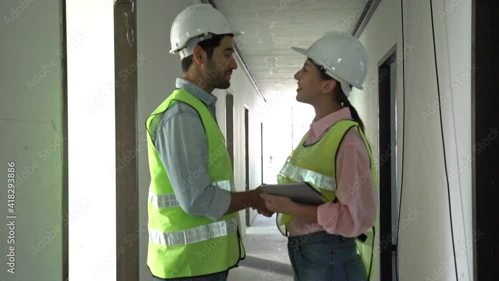 Builder caucasian, asian contractor, engineer man and woman greeting handshake, discussing, inspecting, wearing safety helmets in construction building, apartment at site.Industrial teamwork concept. Builder caucasian, asian contractor, engineer man and woman greeting handshake, discussing, inspecting, wearing safety helmets in construction building, apartment at site.Industrial teamwork concept.