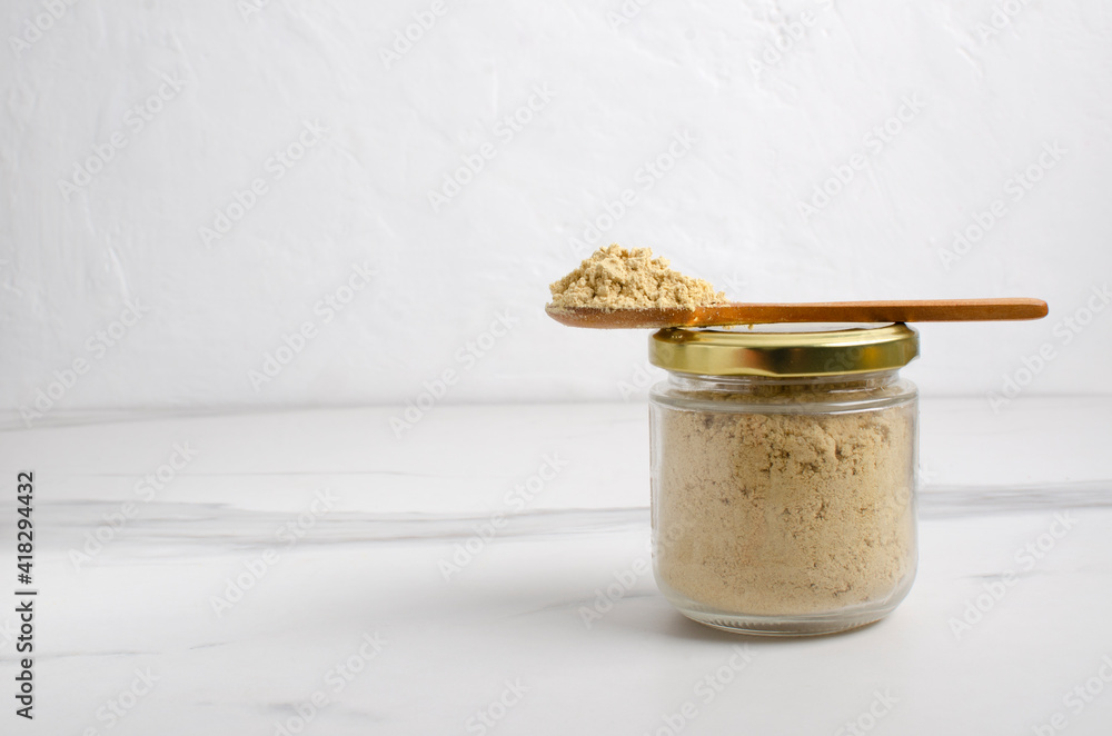Closeup of glass jar full of mustard powder on the white table against bright wall.Empty space Closeup of glass jar full of mustard powder on the white table against bright wall.Empty space