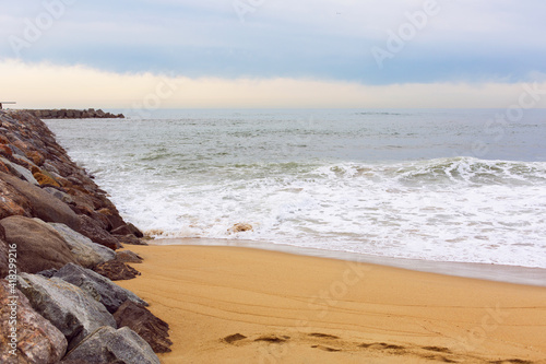 Sea view from the coastal strip of the Mediterranean Sea with a breakwater and sandy beach in the area of San Martí in Barcelona, Spain