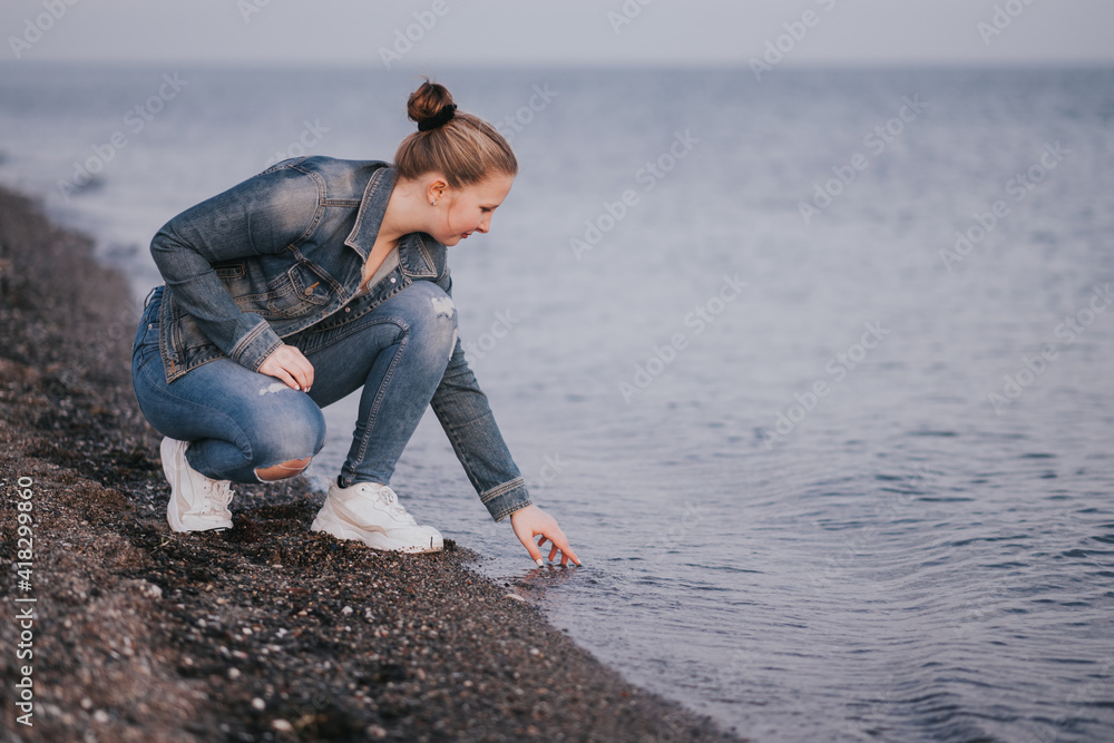 Stockfoto junge Frau in Jeans sitzt, hockt am Meer und hält ihre Hand im  Wasser. stille Zeit, Metime | Adobe Stock