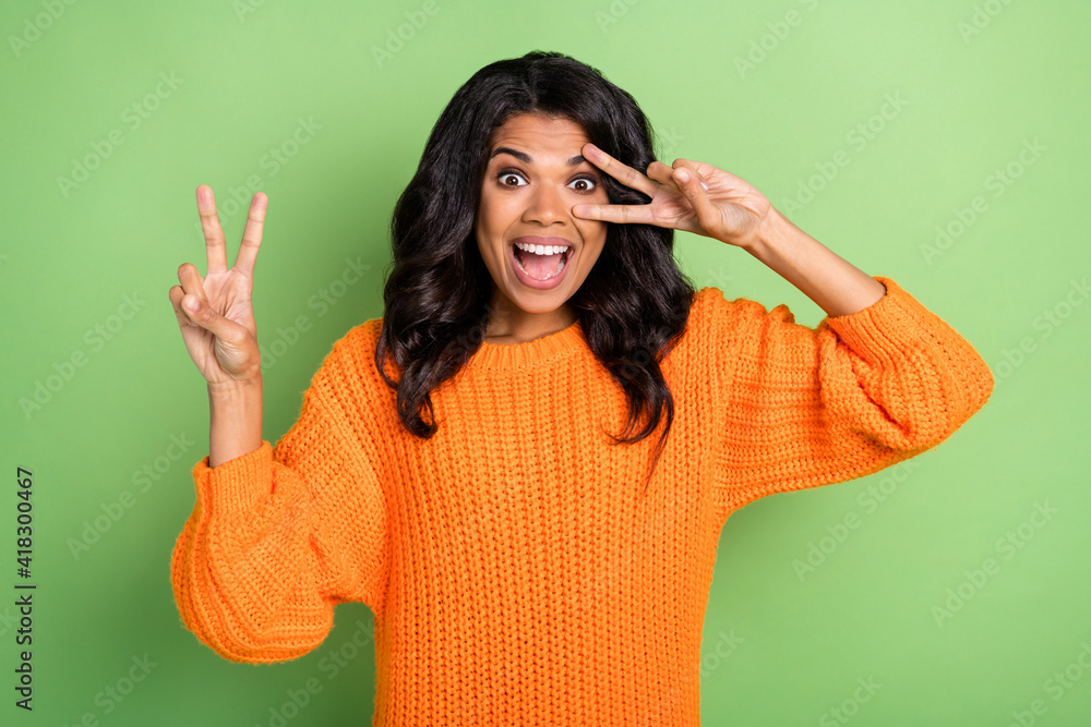 Photo of adorable pretty dark skin woman wear orange sweater showing v-sign cover eye isolated green color background Photo of adorable pretty dark skin woman wear orange sweater showing v-sign cover eye isolated green color background
