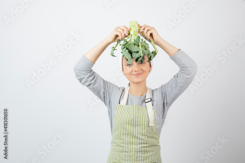 Young beautiful woman in apron posing with fresh broccoli on white background