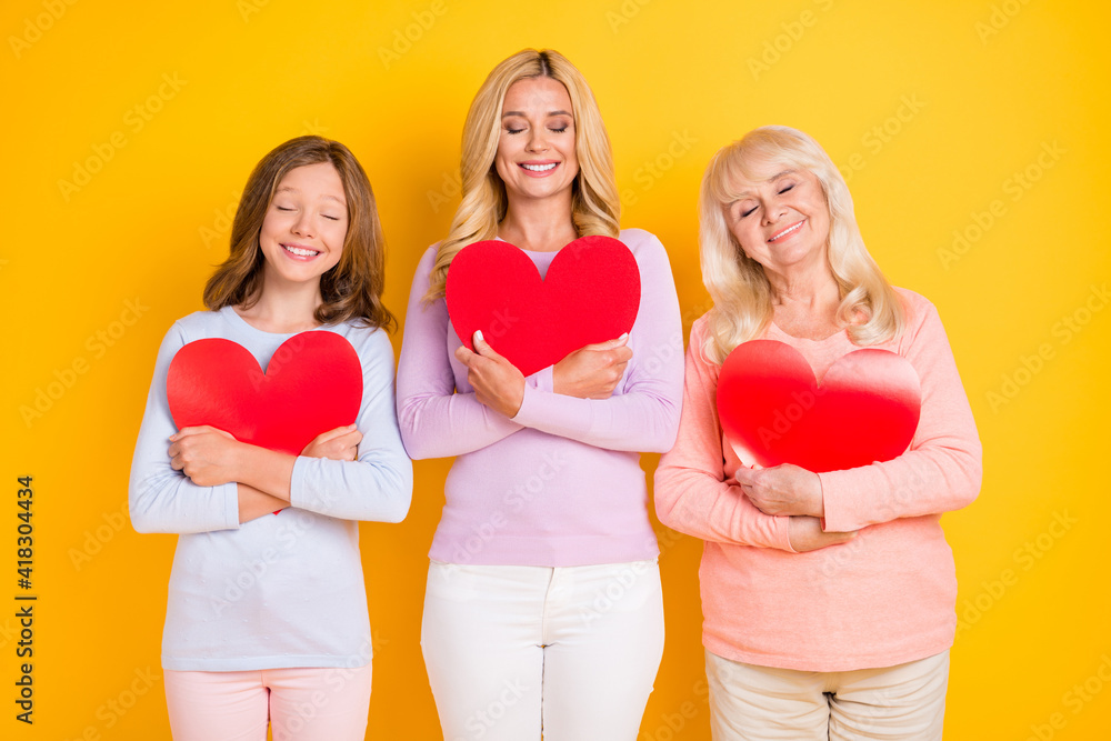 Photo of peaceful grandmother mom and daughter hug heart calm generation isolated on yellow color background Photo of peaceful grandmother mom and daughter hug heart calm generation isolated on yellow color background