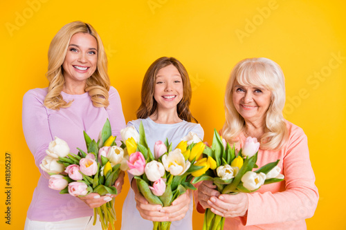 Photo of happy retired pensioner old woman little girl and young mother give you tulips isolated on yellow color background