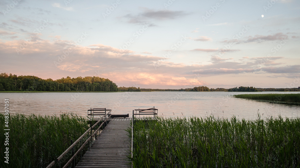 Naklejka premium Beautiful evening view with lake Ezezers, wooden footbridge and sunlit trees, Latvia.