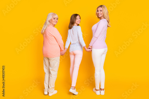 Full size back photo of optimistic three woman grand mom daughter go look wear pastel cloth isolated on yellow background