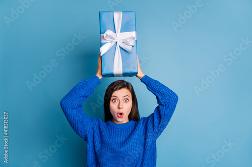 Photo of young attractive lovely shocked amazed surprised girl hold new year present above head isolated on blue color background © deagreez