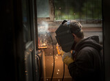 a welder in a welding mask, gloves welds metal with a welding machine and an electrode in his hand, sparks fly, a beautiful glow, bokeh, orange light on a black background, a flash of light and smoke