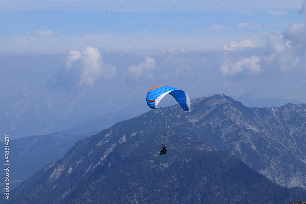 experienced parachutist flies in the right wind and drives a parachute around the Austrian Alps. Paratrooper with a white-blue parachute made of a special fiber. Dangerous sport. Around krippenstein experienced parachutist flies in the right wind and drives a parachute around the Austrian Alps. Paratrooper with a white-blue parachute made of a special fiber. Dangerous sport. Around krippenstein