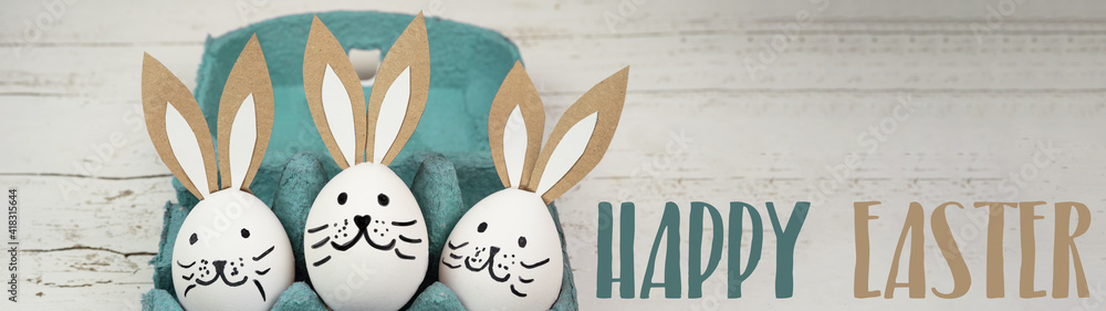Happy Easter background banner panorama greeting card -Close-up from white painted eggs and easter bunny in green turquoise egg carton on rustic white vintage shabby wooden table - obrazy, fototapety, plakaty 