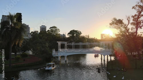 Aerial dolly in of boats sailing under white bridge in Rosedal gardens in Palermo neighborhood at sunset, Buenos Aires photo