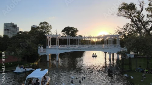 Aerial of ducks and boats sailing under white bridge in Rosedal gardens pond at golden hour, Buenos Aires photo