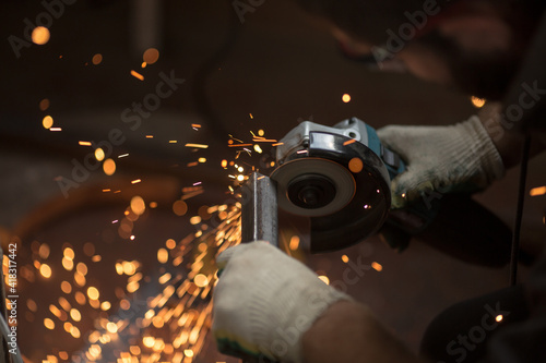 bulgarian angle grinder rotates the disc, a person cuts off the metal profile with his hands, sparks fly, beautiful glow, bokeh, orange light on a black background, production, flash of light