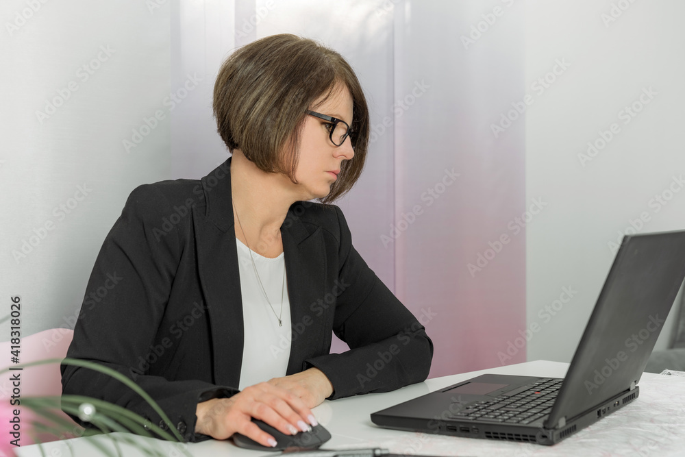 A brunette bussiness woman in glasses in a black jacket works on the computer in the office A brunette bussiness woman in glasses in a black jacket works on the computer in the office