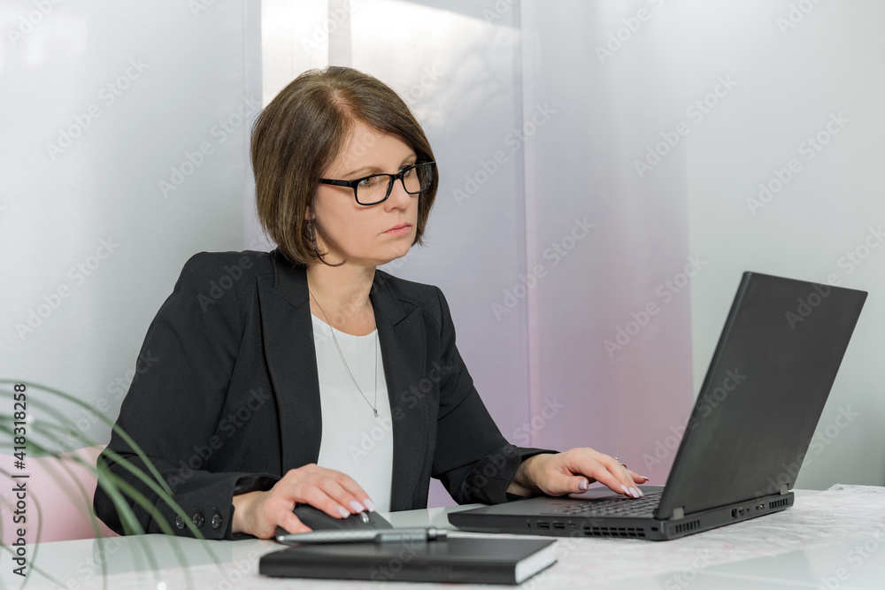 A brunette bussiness woman in glasses in a black jacket works on the computer in the office A brunette bussiness woman in glasses in a black jacket works on the computer in the office