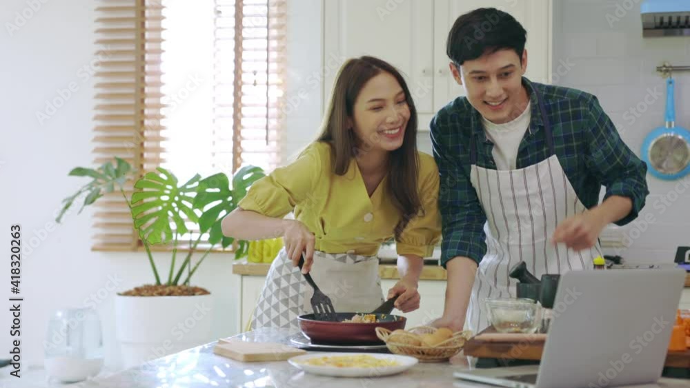 Young married couple Cooking breakfast By looking at how to make a laptop computer with a happy expression In their own home Young married couple Cooking breakfast By looking at how to make a laptop computer with a happy expression In their own home