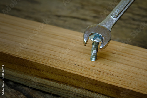 Close-up wrench screwing nut a furniture screw into a wooden plank, The effort  wrong of tools as a fail concept