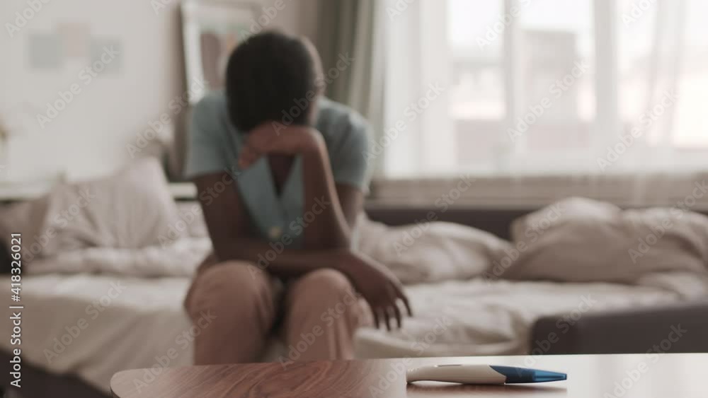Lockdown of unrecognizable African-American woman sitting on bed in bedroom and crying because of negative pregnancy test result Lockdown of unrecognizable African-American woman sitting on bed in bedroom and crying because of negative pregnancy test result