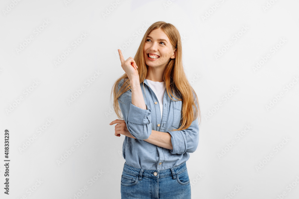 young woman points finger up in copy space while standing over white background young woman points finger up in copy space while standing over white background