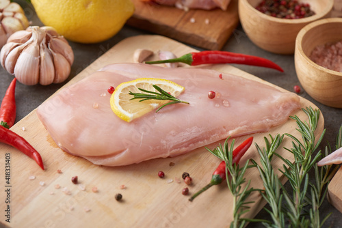 raw chicken fillet with garlic, pepper and rosemary on wooden on chopping board. fresh fillet. fresh chicken meat, chicken fillet with spices at black stone table. top view with copy space..