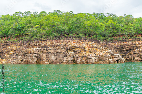 Rock walls of on the shore of the Lake of Furnas, Capitólio MG, Brazil. Green water of the lake, sedimentary rocks and the vegetation growing up the rocks.  photo