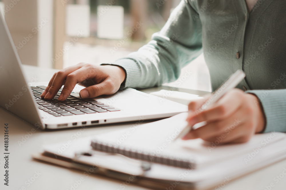 Business women work on computers and write on notepad with pen to calculate financial statements within the office. Business women work on computers and write on notepad with pen to calculate financial statements within the office.