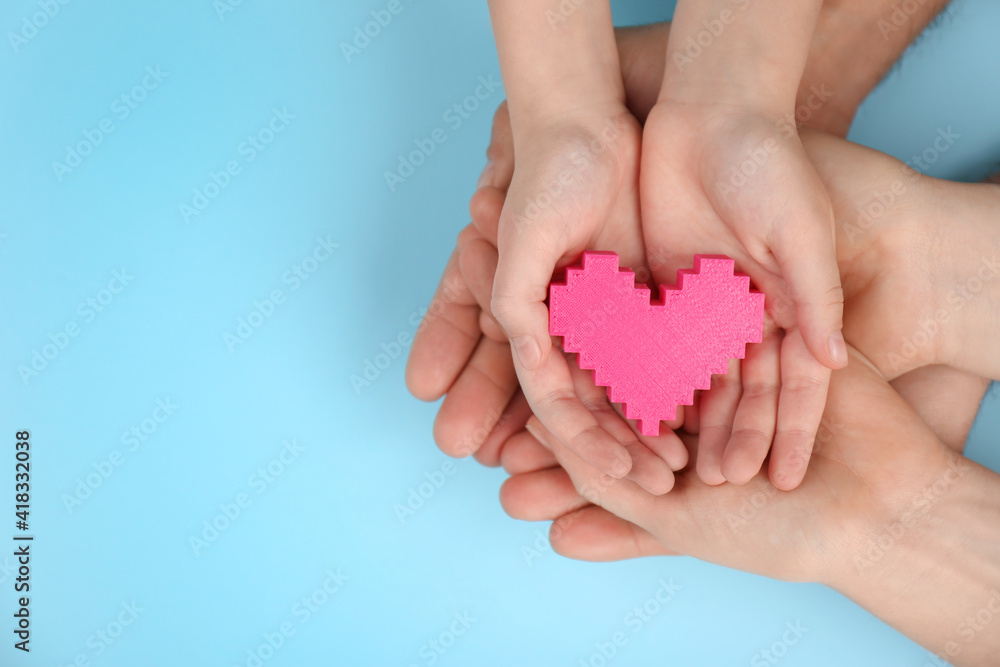 Top view of parents and kid holding pink heart in hands on turquoise background, space for text. Family day Top view of parents and kid holding pink heart in hands on turquoise background, space for text. Family day