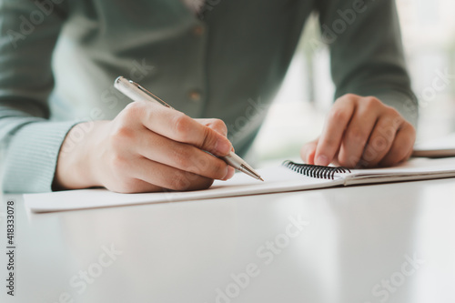 Business women work on computers and write on notepad with pen to calculate financial statements within the office.