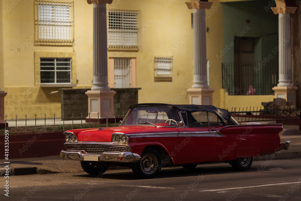 Amazing old american car on streets of Havana with colourful buildings in background during the night. Havana, Cuba.