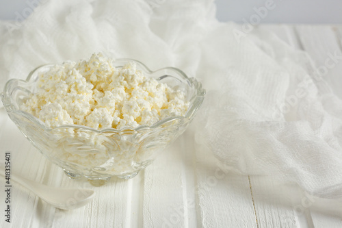 Cottage cheese in a glass bowl. On a white wooden table