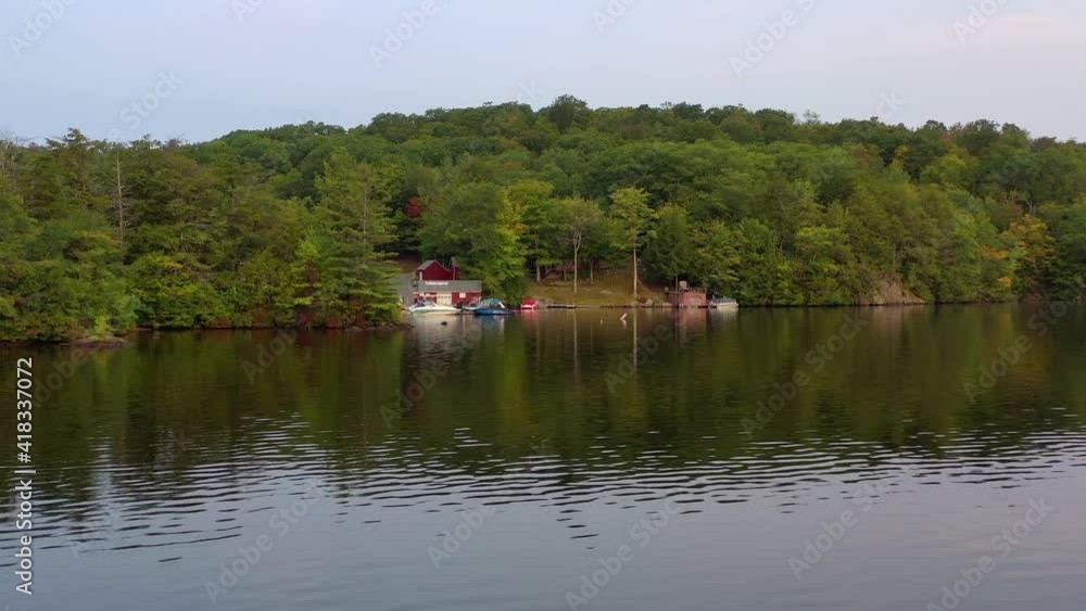 Aerial shot of boats moored at lakeshore against trees, drone flying backward over lake against sky - Berkshire County, Massachusetts Aerial shot of boats moored at lakeshore against trees, drone flying backward over lake against sky - Berkshire County, Massachusetts