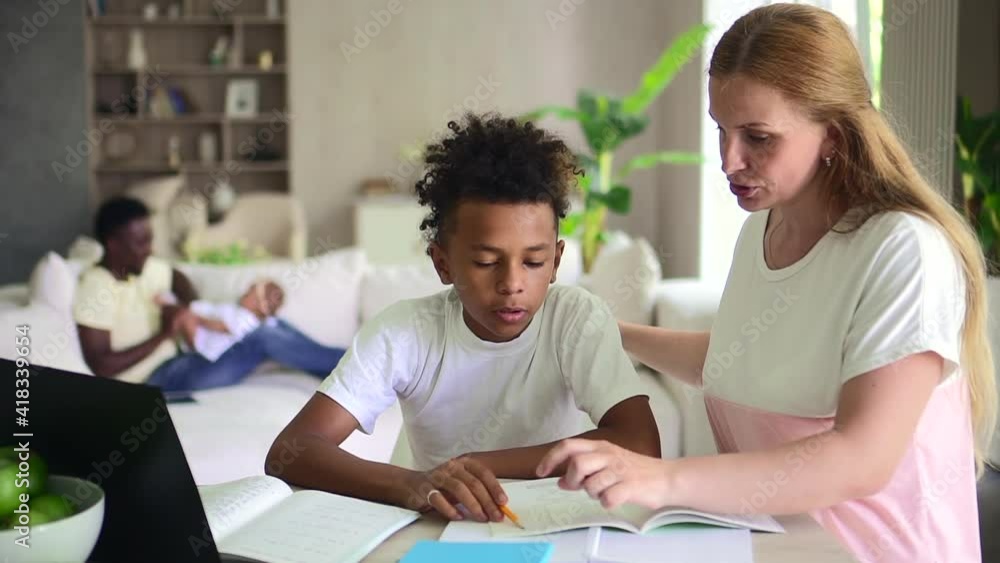 Woman and boy doing homework while sitting at table with computer in apartment room spbd. Young mother helps son to study, talks and sits at desk with laptop, dad plays with his little daughter on Woman and boy doing homework while sitting at table with computer in apartment room spbd. Young mother helps son to study, talks and sits at desk with laptop, dad plays with his little daughter on