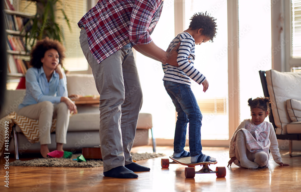 Fototapeta premium A young father helping his son riding the skateboard at home. Family, together, love, playtime