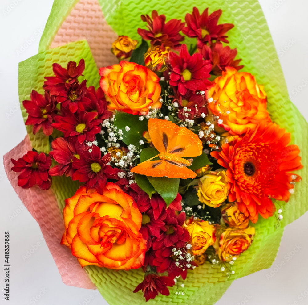 Obraz premium Bouquet of yellow-orange Roses, orange Gerbera and red Chrysanthemums with a plastic butterfly close - up in a package on a white background