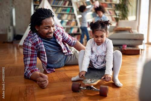 A young father pushing his little daughter on the skateboard at home. Family, together, love, playtime