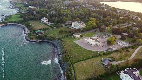 Aerial panning shot of houses by waves splashing on coastline, drone flying forward over city by sea at sunset - Newport, Rhode Island photo