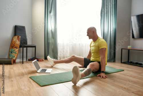Exercising online. Mature personal fitness conducting online training while sitting on yoga mat at home in the living room © Svitlana