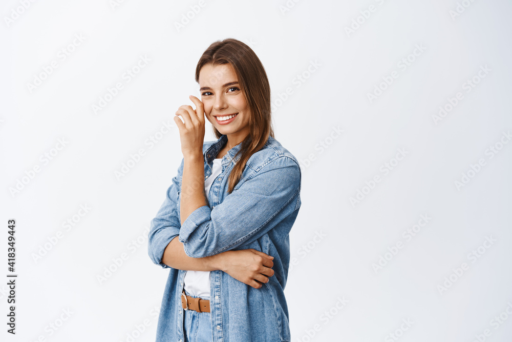 Beauty and skin care. Beautiful blond girl touching her face and smiling white teeth, standing half turned against white background in casual clothes Beauty and skin care. Beautiful blond girl touching her face and smiling white teeth, standing half turned against white background in casual clothes