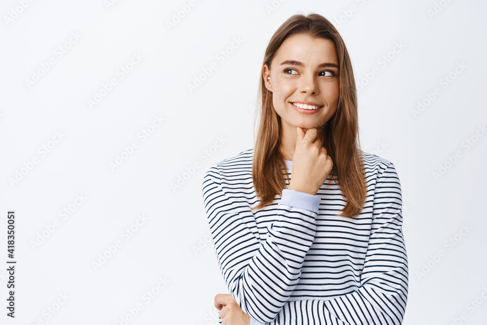 Portrait of thoughtful girl making assumption, having interesting ideas, looking left at copy space logo and smiling, pondering, standing over white background Portrait of thoughtful girl making assumption, having interesting ideas, looking left at copy space logo and smiling, pondering, standing over white background