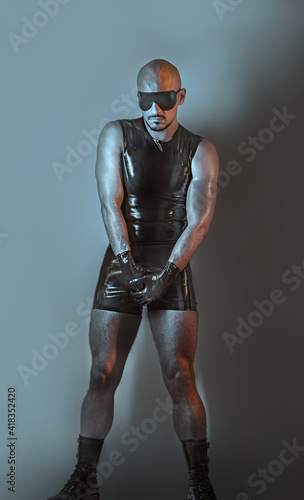 Dark creative artistic portrait of a rubber fetish, latex young man with fashion rubber outfit on a mysterious background.