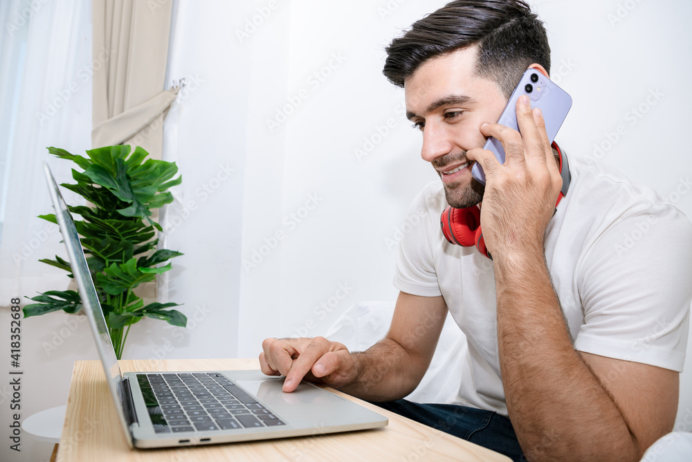 Portrait of handsome man using smartphone and laptop computer over white background in the bedroom. Showing and presented impressions looking big project. Portrait of handsome man using smartphone and laptop computer over white background in the bedroom. Showing and presented impressions looking big project.