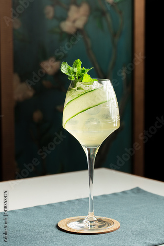 Cocktail in wine glass with alcohol, cucumber slices and ice cubes on the table at restaurant
