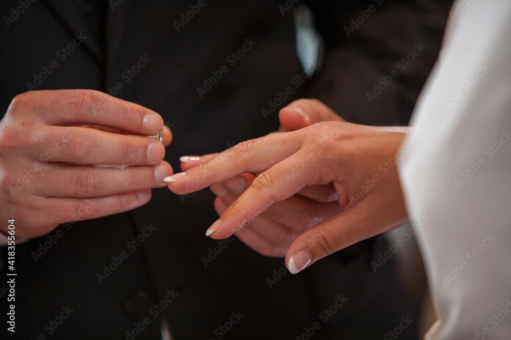 Fototapeta premium Close up of loving bride and groom putting a beautiful wedding ring to the beloved partner, marry me concept. High quality photo