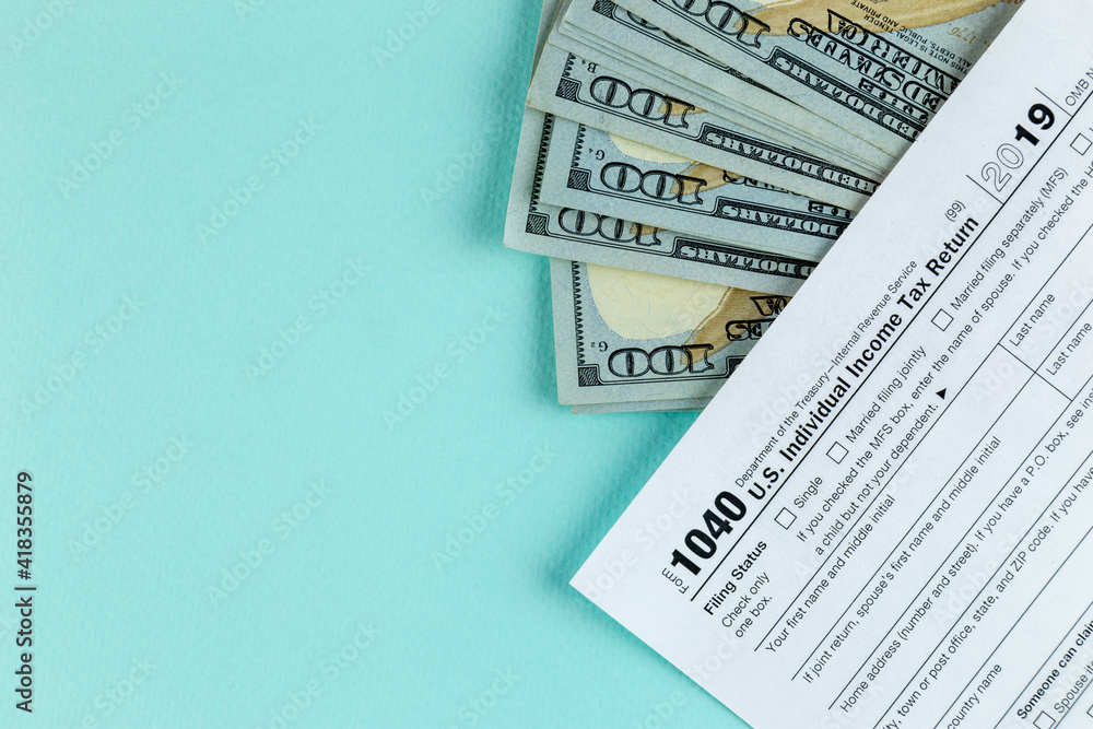 Naklejka premium Tax return concept. Still life of US individual Income Tax Form 1040 pen and inscription text on wooden blocks with several 100 dollar banknotes on a blue pastel background
