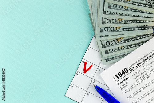 Tax return concept. Still life of US individual Income Tax Form 1040 pen and inscription text on wooden blocks with several 100 dollar banknotes on a blue pastel background