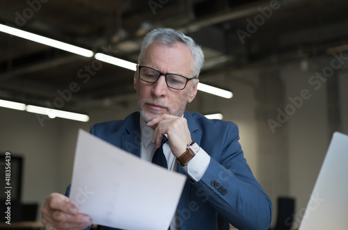 Fotografija Pensive senior businessman reading contract working in modern office