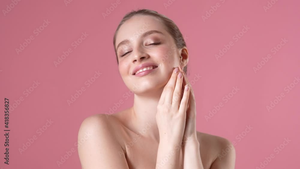 A smiling young woman is posing to the camera while standing isolated over pink background in studio A smiling young woman is posing to the camera while standing isolated over pink background in studio
