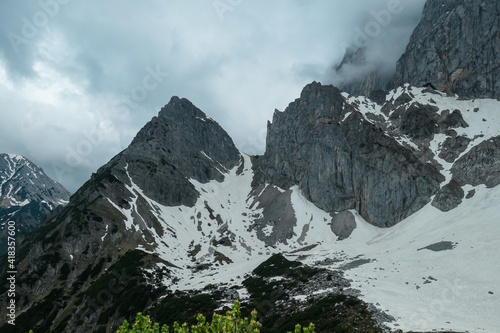 A panoramic view on the Alpine peaks in Austria from Marstein. The slopes are mostly covered with snow. Stony and sharp mountains. Overcast. Baren slopes, green valley below. Serenity and calmness photo