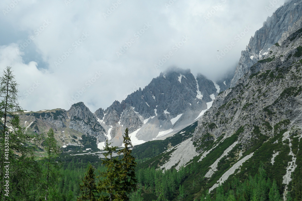 A panoramic view on the Alpine peaks in Austria from the Marstein. The slopes are still partially covered with snow. Stony and sharp mountains. Overcast. Baren slopes, dense forest at the foothill.