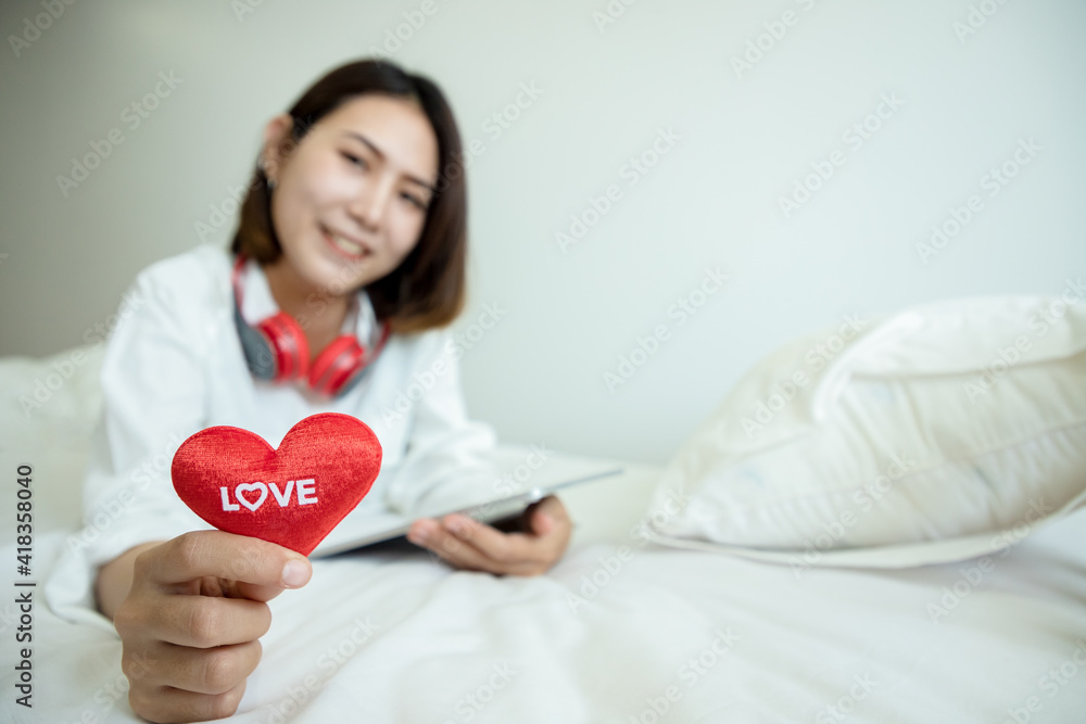 Asian beautiful woman using tablet for buy gifts on Valentine's Day and showing hearts love text on bedroom. Seasonal Holiday concept.